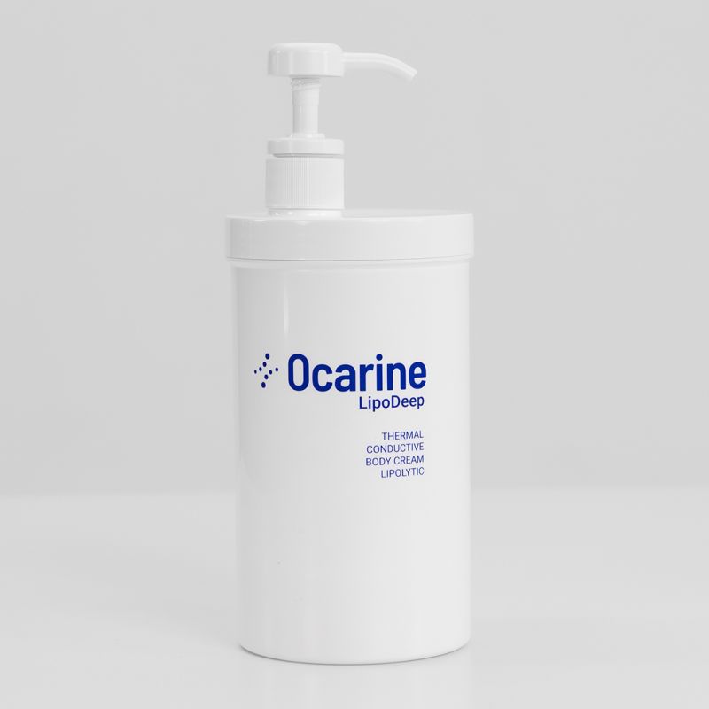 A woman is preparing a treatment table in what appears to be a spa or medical setting. She is adjusting a sheet or roll of paper on the table. Shelves behind her are stocked with various bottles, likely skincare or medical products. A large adjustable lamp is attached to the workspace.